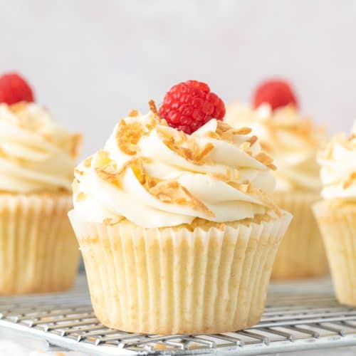 Coconut cupcakes with coconut frosting, decorated with toasted coconut on a cooling rack