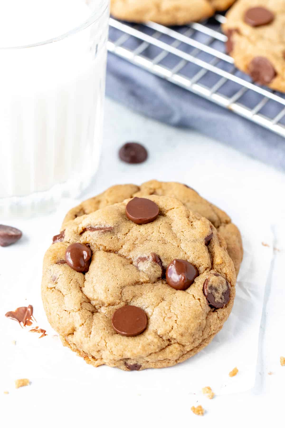 Soft chocolate chip cookie, resting on a second cookie with a glass of milk