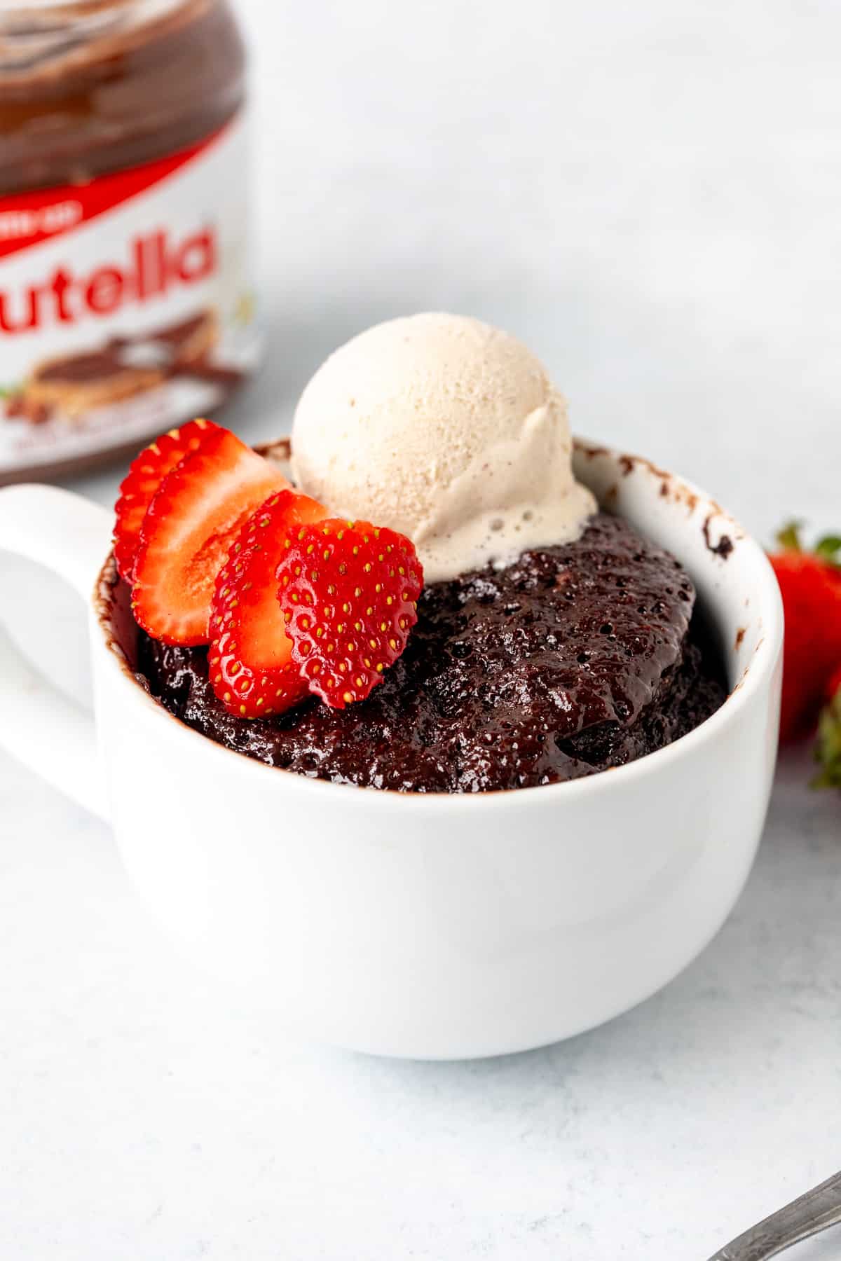 Nutella mug cake topped with a scoop of ice cream and strawberry slices