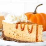 Slice of no bake pumpkin cheesecake topped with whipped cream and a drizzle of caramel sauce