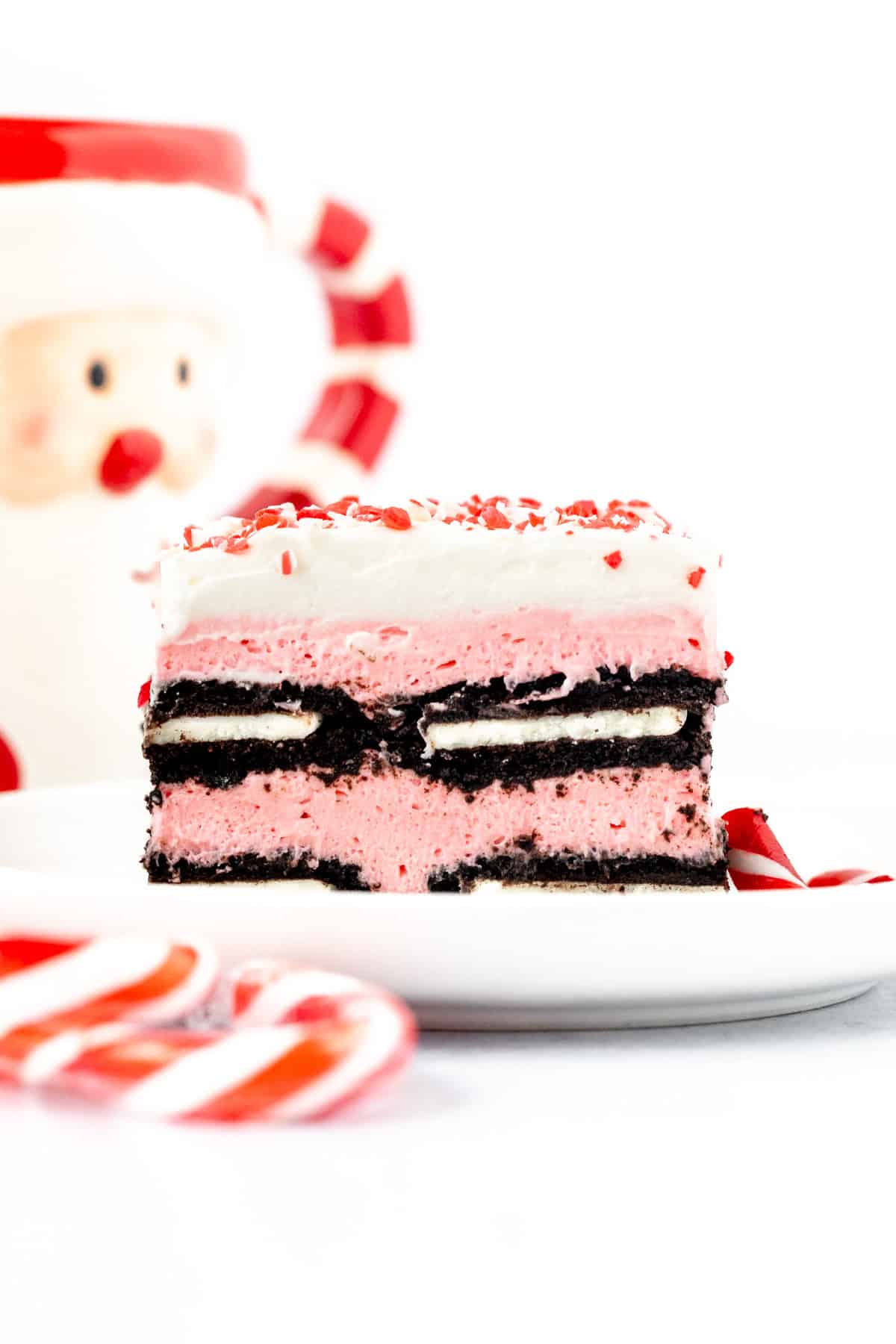 Slice of candy cane icebox cake, with layers of pink no bake cheesecake filling and Oreo cookies, topped with whipped cream and crushed candy canes