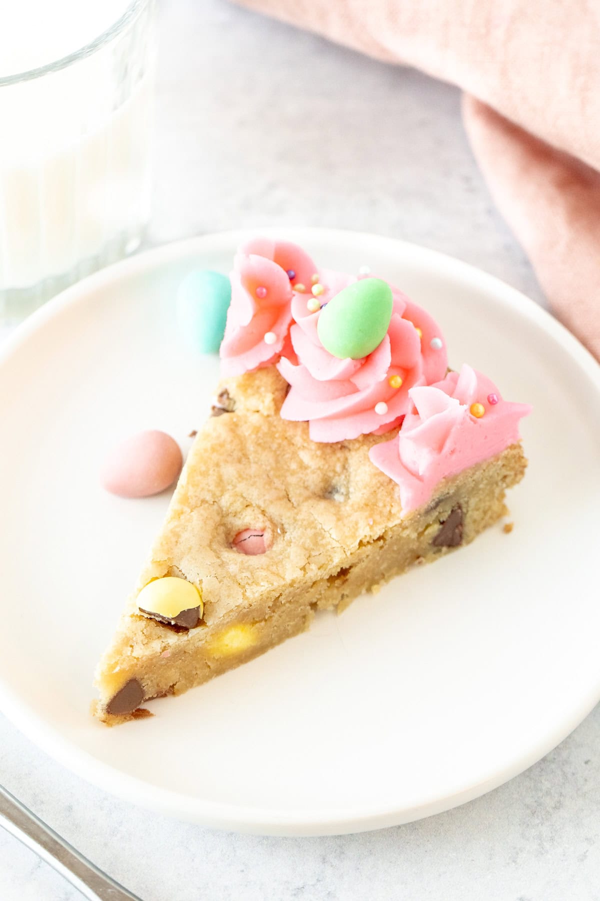 Slice of Easter cookie cake decorated with pink frosting and a chocolate egg candy