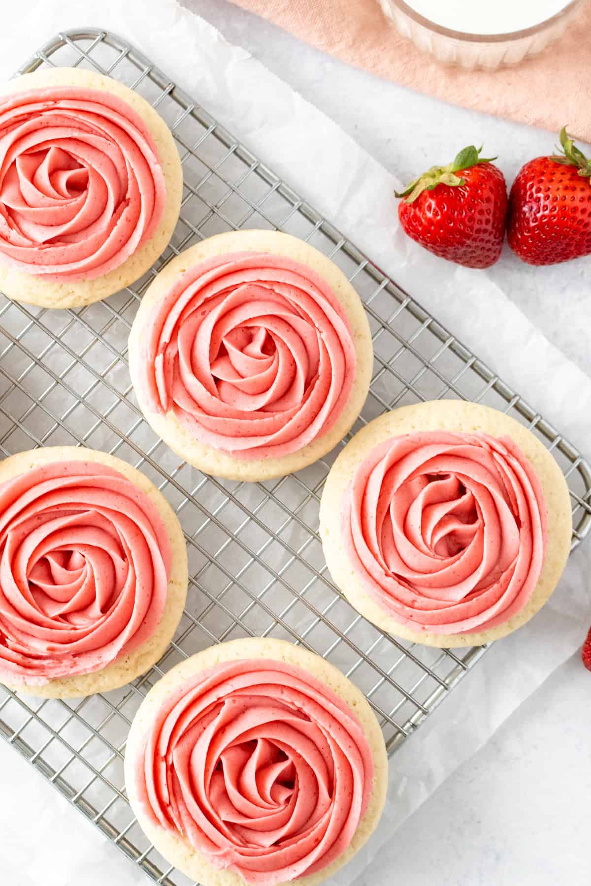 Sugar cookies with strawberry frosting on a cooling rack
