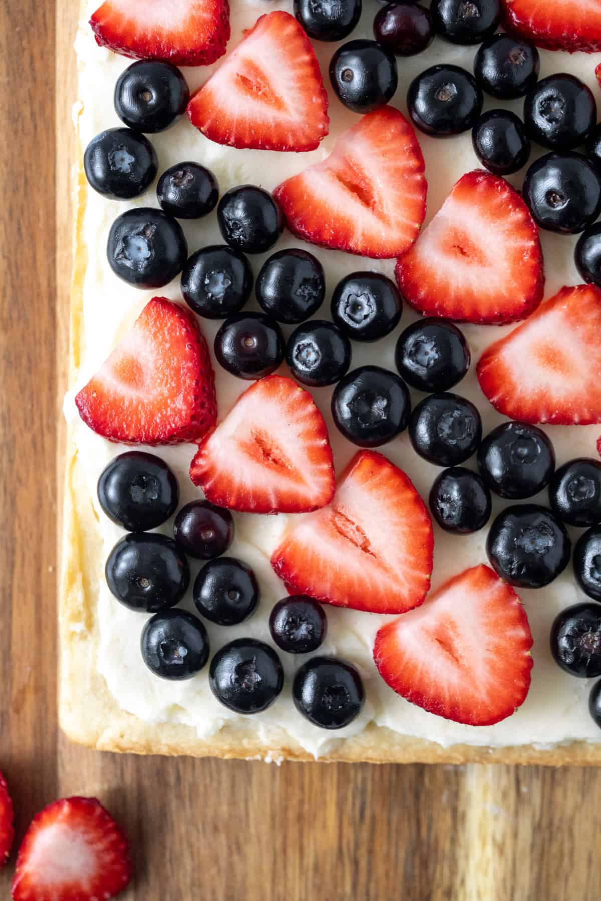 Slab of sugar cookie bars with vanilla frosting and topped with blueberries and sliced strawberries