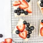 Sugar cookie bars topped with vanilla frosting and fresh berries on a cooling rack