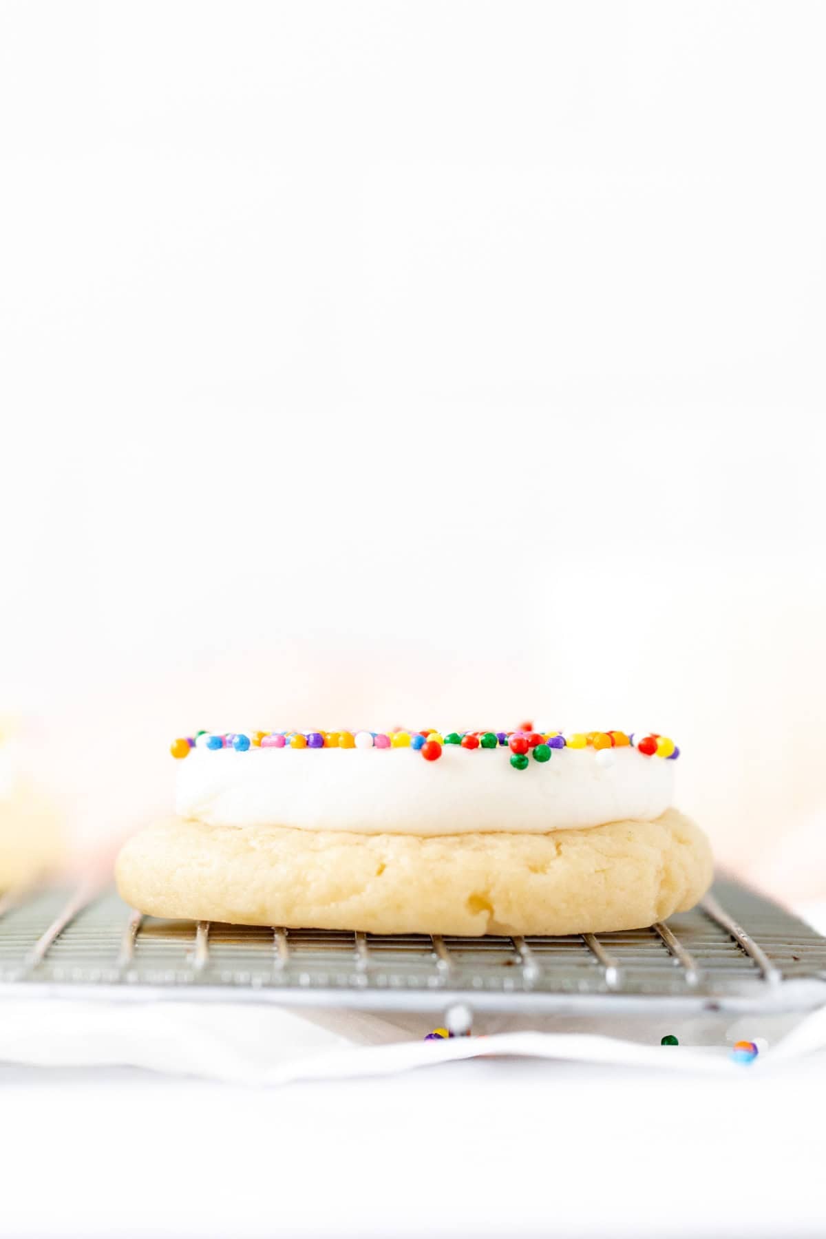 Dot cake cookie on a cooling rack with a thick layer of vanilla frosting and sprinkles on top