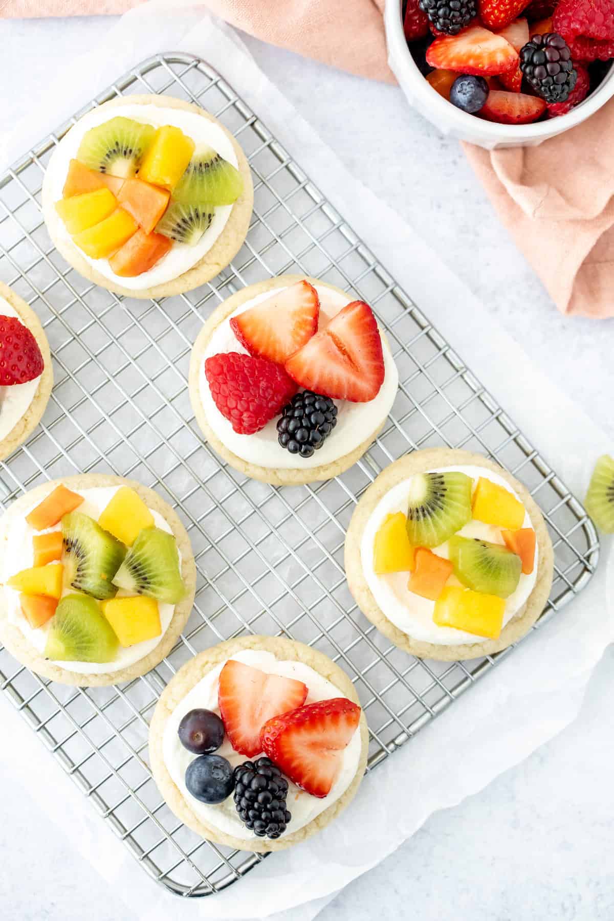 Mini fruit pizzas with cream cheese topping and fresh fruit on top, on a cooling rack