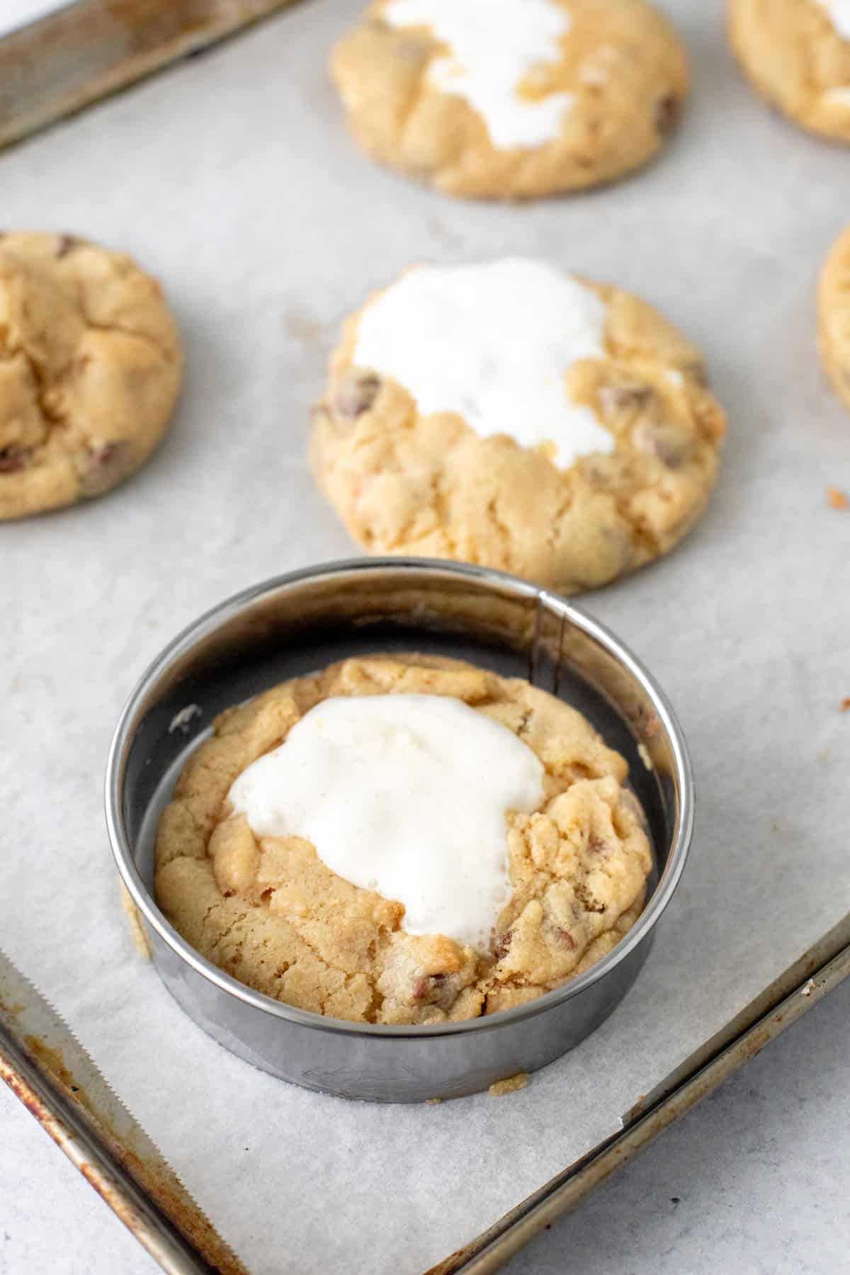 S'mores cookies on a cookie sheet with a round cookie cutter around the cookie.