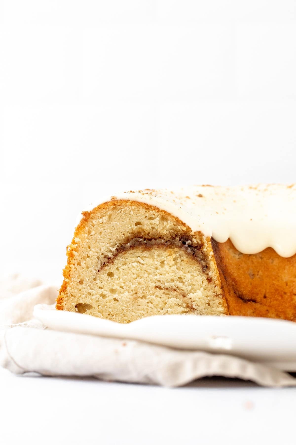 Cinnamon swirl bundt cake with cream cheese icing on a white plate, withe slices cut out of the bundt cake