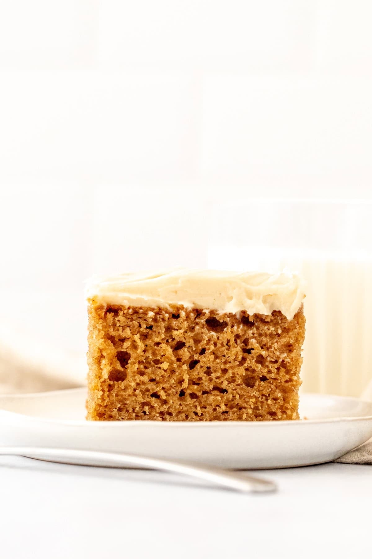 slice of spice cake topped with cream cheese frosting with a glass of milk