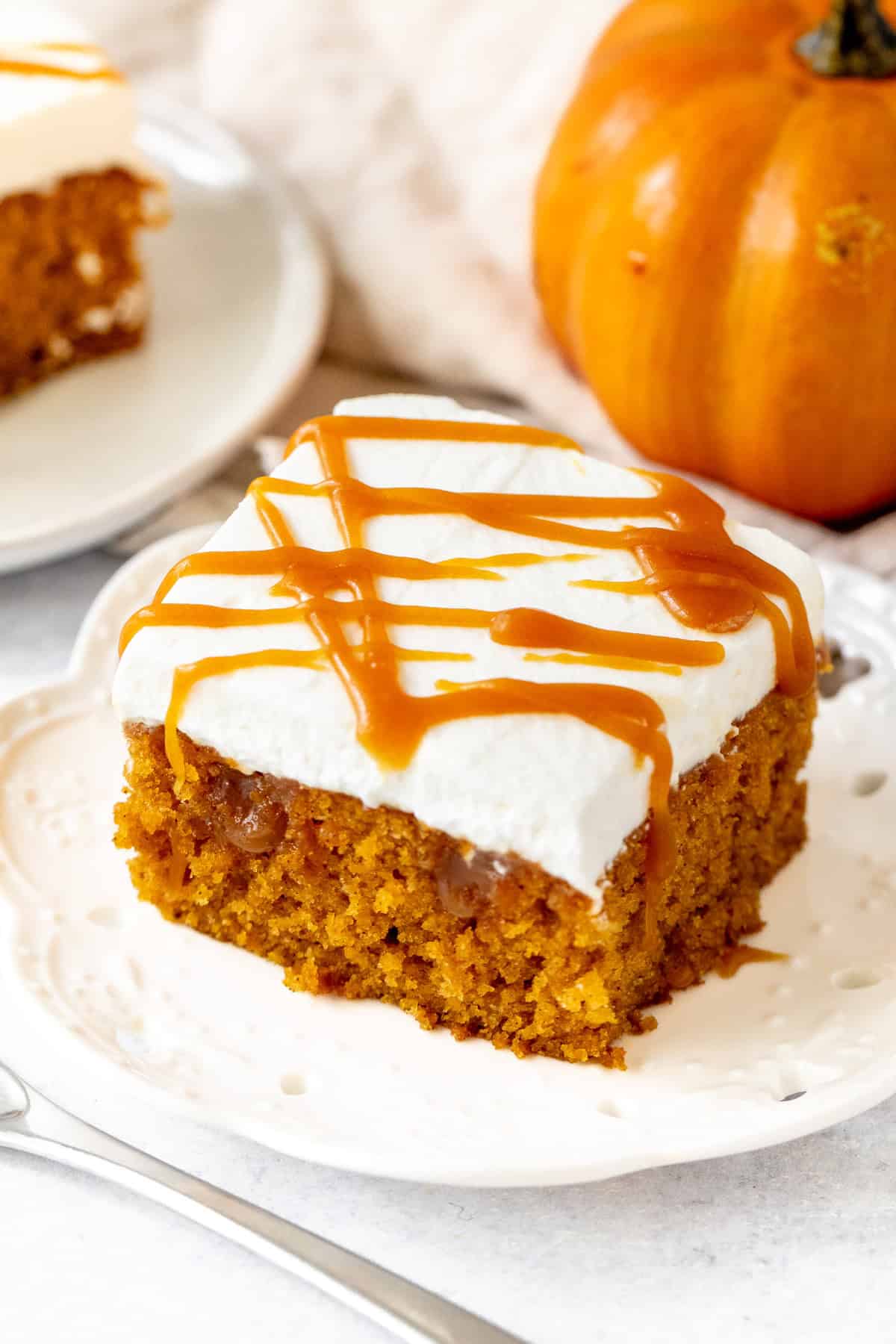Slice of pumpkin poke cake topped with whipped cream and caramel